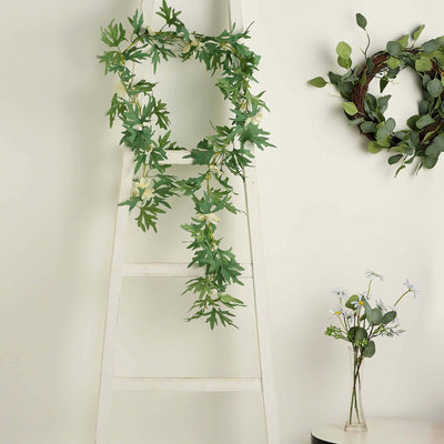 Artificial greenery garland hanging on a ladder against a neutral wall.