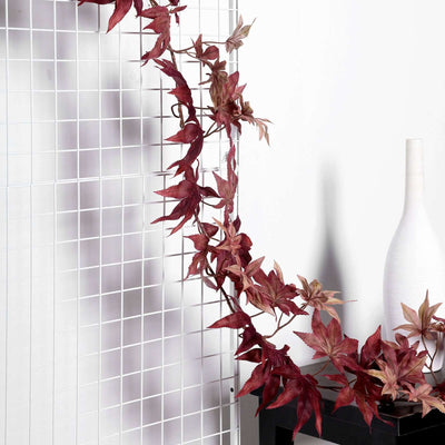 Artificial red maple leaf garland on a grid backdrop.