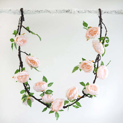 Pink flower garland hanging on a branch with green leaves