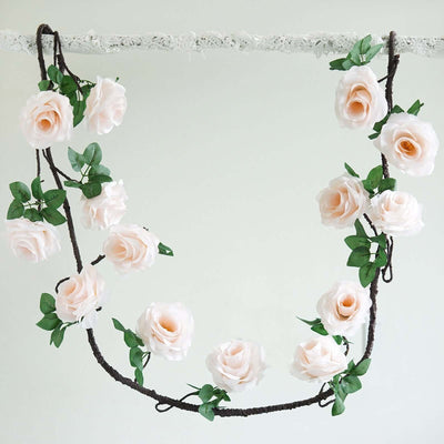 Pink rose garland with green leaves hanging on a white background.