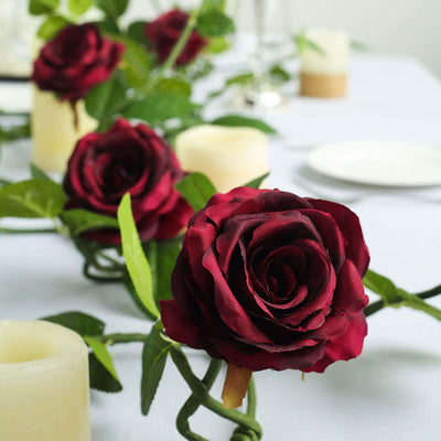 Silk red roses on a table with candles and greenery.
