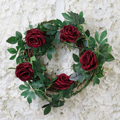 Red rose wreath adorned with greenery against a floral background.