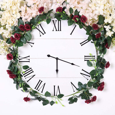 Floral wall clock with black Roman numerals and green leaves on a white background