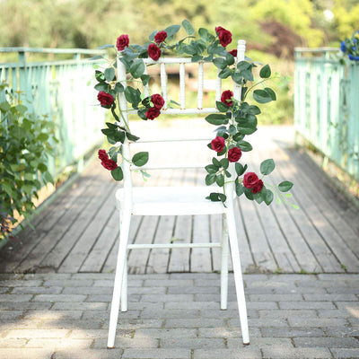White chair adorned with red roses and greenery on a garden pathway.