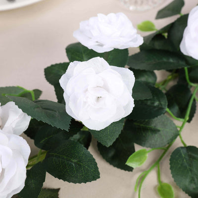 Artificial white rose flowers with green leaves on a beige surface.