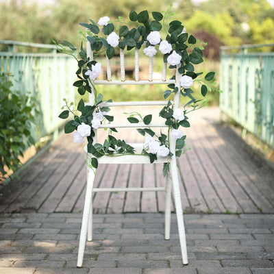 White chair adorned with white roses and greenery on a garden pathway.