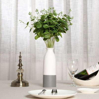 Modern vase with greenery centerpiece on a dining table.