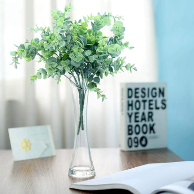 Artificial green plant in a clear vase on a wooden table.