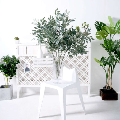 Artificial eucalyptus leaves in a glass vase on a white chair.