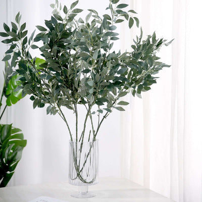 Artificial green leafy plant in a clear vase on a table.