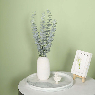 Eucalyptus plant in a white vase on a marble tray with framed art.