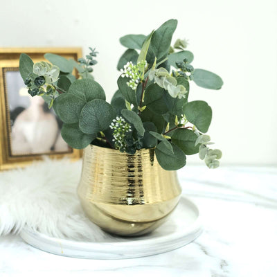 Gold vase with greenery and eucalyptus arrangement on a marble surface.
