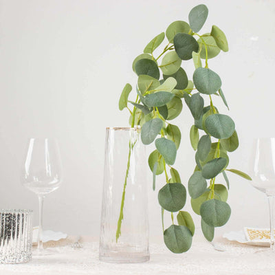 Eucalyptus branch in a clear vase on a dining table setting with glassware.