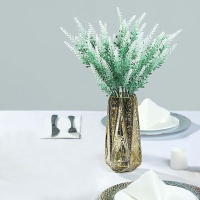 Gold geometric vase with green and white faux flowers on a dining table.
