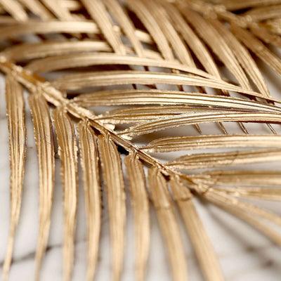 Gold palm leaf close-up on a marble surface.