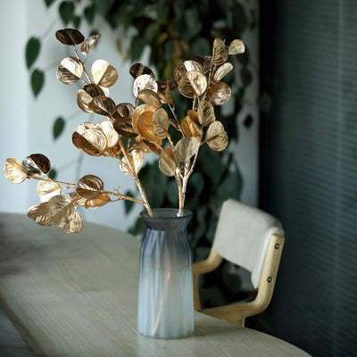 Gold leaf branches in a vase on a wooden table.