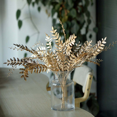 Gold foliage arrangement in a glass vase on a wooden table.
