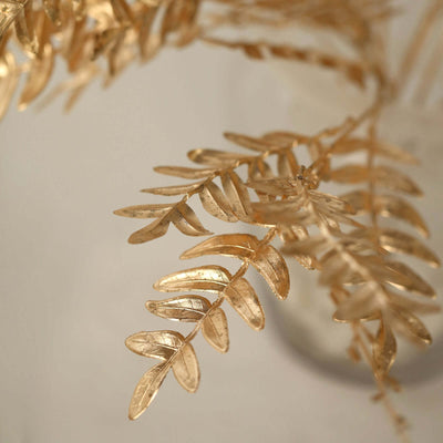 Gold leaf branch in a clear vase, showcasing intricate details and textures.