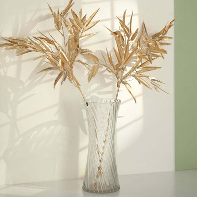 Elegant glass vase with dried golden leaves against a soft background.