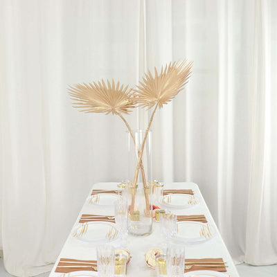 Elegant table setting with gold palm leaves and glassware on a white tablecloth.