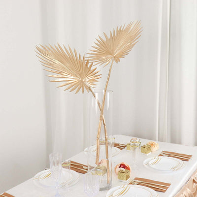 Gold palm leaf decor in a stylish vase on a dining table setting.