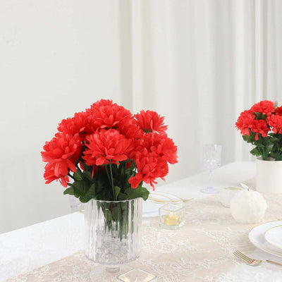 Red artificial flowers in a clear vase on a beautifully set dining table.