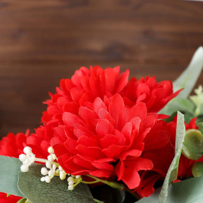 Red artificial flowers with green leaves against a wooden background.