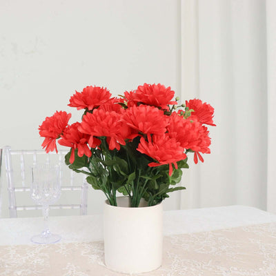 Red artificial flowers in a white vase on a table.