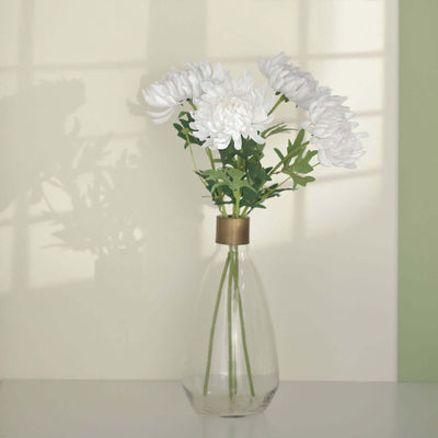 White artificial flowers in a clear vase against a soft green wall.