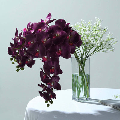 Purple orchids and white flowers in a glass vase on a table.