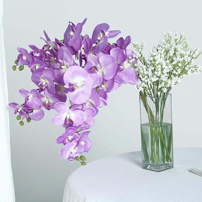 Purple orchids and white flowers in a clear vase on a table.