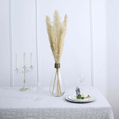Pampas grass arrangement in a glass vase on a dining table setting.