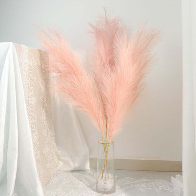 Pink pampas grass in a glass vase against a neutral background.
