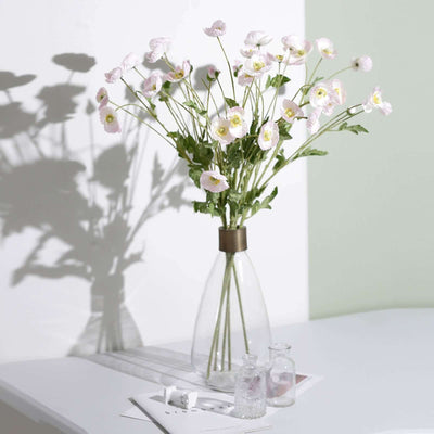 Artificial pink flowers in a clear vase on a white table.