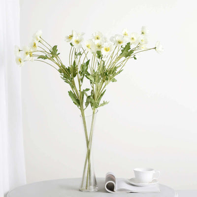 White flowers in a vase on a table with a cup and magazine.