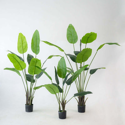 Artificial tropical plants in black pots, showcasing vibrant green leaves.