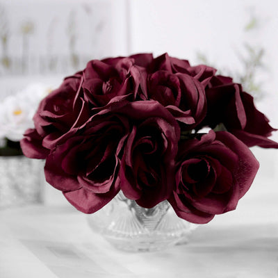Artificial burgundy rose bouquet in a clear glass vase.