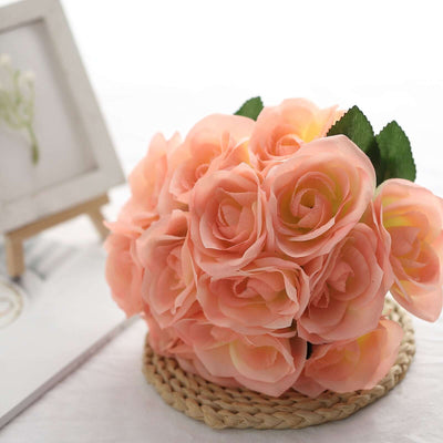 Peach artificial roses bouquet on a woven mat with a small easel frame in the background.