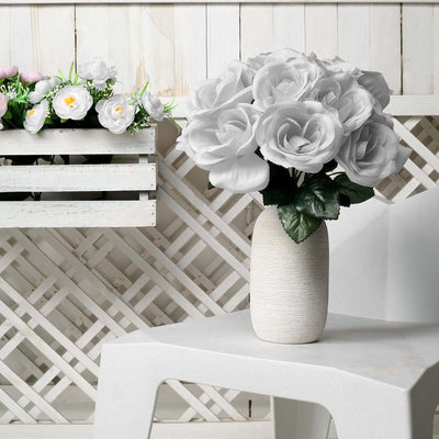 White rose bouquet in a textured vase on a white table.
