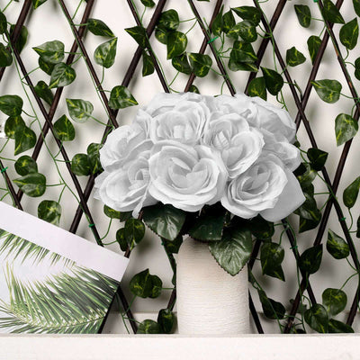 White rose bouquet in a textured vase against a green backdrop.