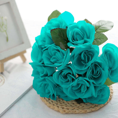 Teal artificial rose bouquet with green leaves in a woven basket.