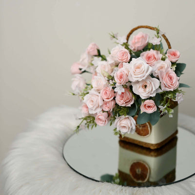 Pink rose bouquet in a decorative basket on a mirrored table.