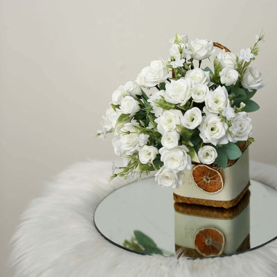 White rose flower arrangement in a decorative basket on a mirrored table.