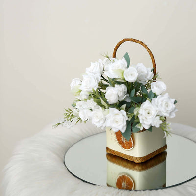 White roses in a decorative basket on a mirrored surface.