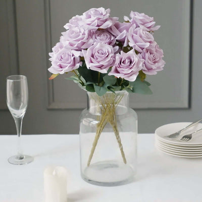 Lavender artificial roses in a clear glass vase on a table setting.