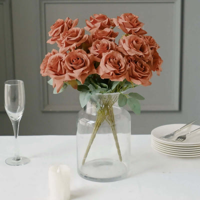 Peach-colored roses in a clear vase on a table setting.