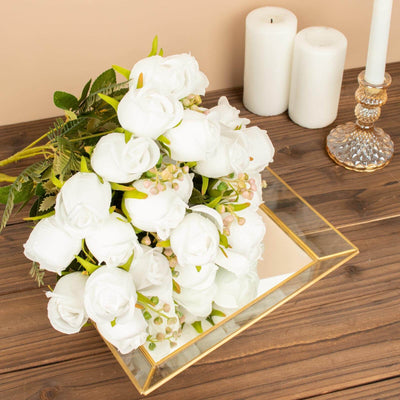 White artificial roses in a decorative mirror box with candles and a candle holder.