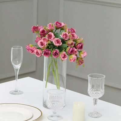 Pink roses in a clear vase on a dining table with glassware.