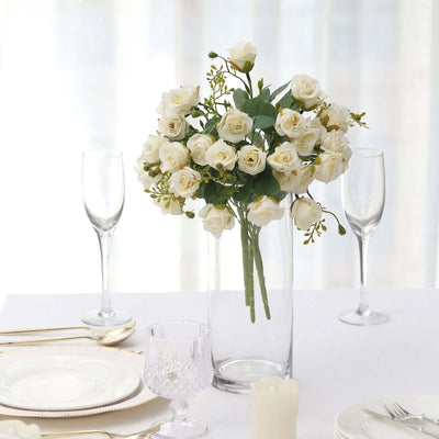 White rose bouquet in a clear vase on a dining table setting.