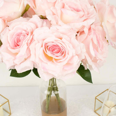 Pink artificial roses in a clear vase on a white table.